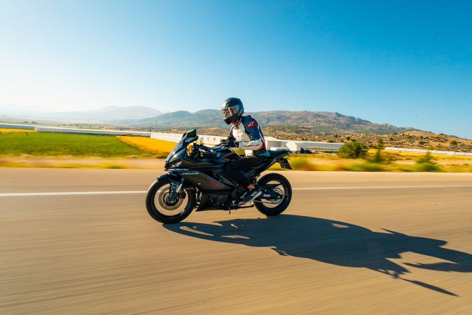 A biker rides a motorcycle at high speed on an open road with scenic landscape views.