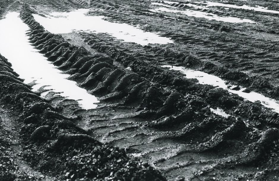 Detailed close-up of muddy tire tracks filled with water, capturing texture and patterns.